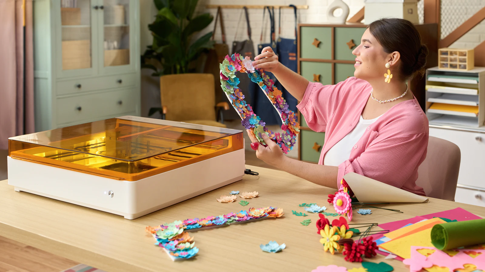 An xTool M2 laser cutter beside a maker assembling a colourful paper flower frame