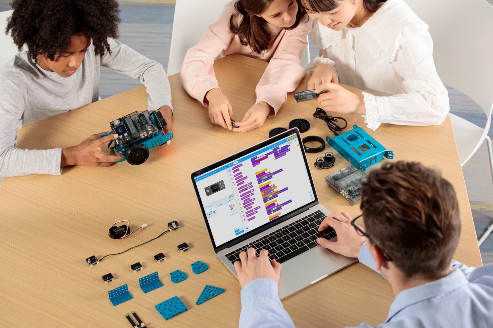 Students building and programming mBot2 robots around a classroom table