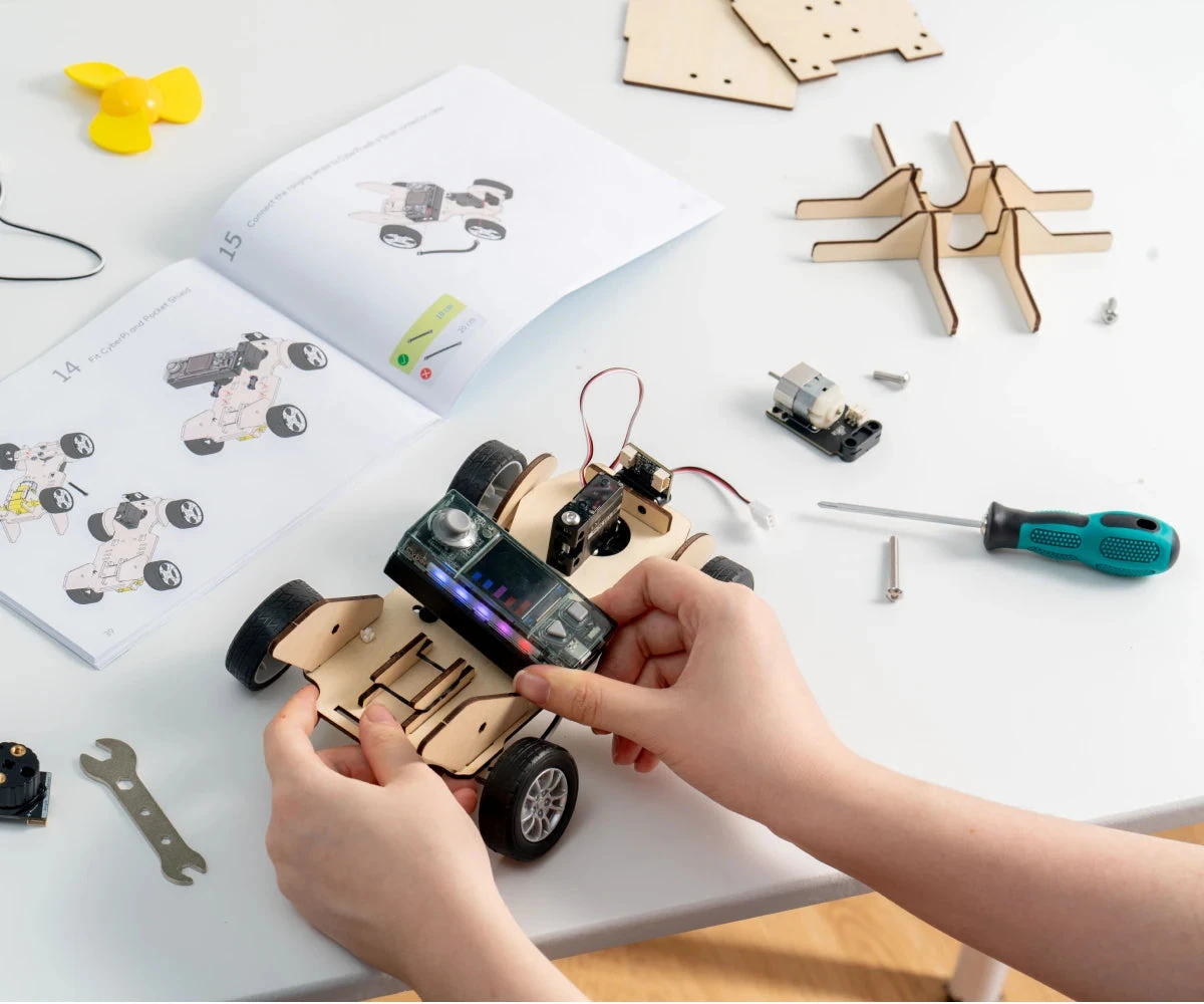 Hands building a wooden wheeled project around a CyberPi controller.