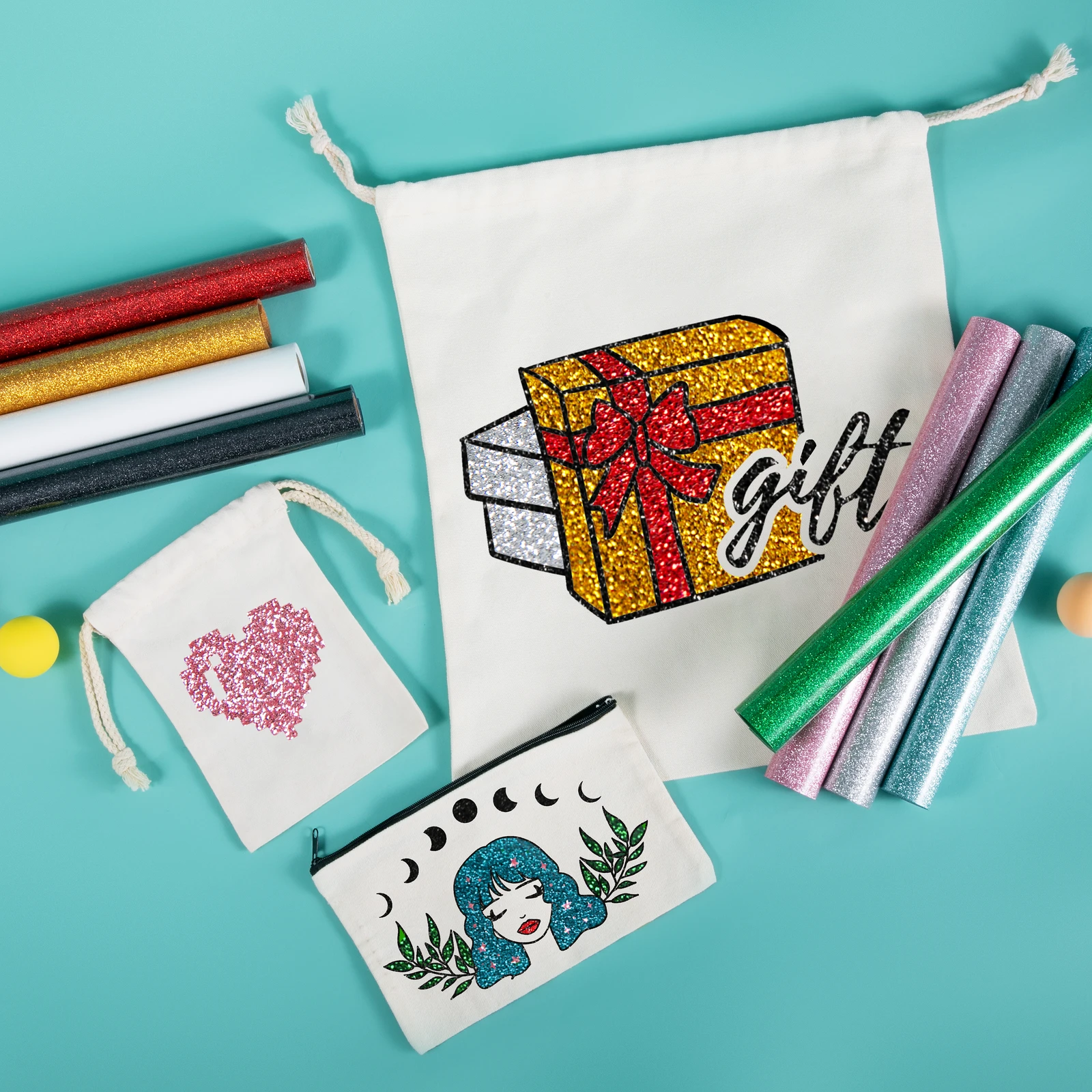 Drawstring bags and a fabric pouch decorated with colourful glitter vinyl designs, surrounded by vinyl rolls on a turquoise background.