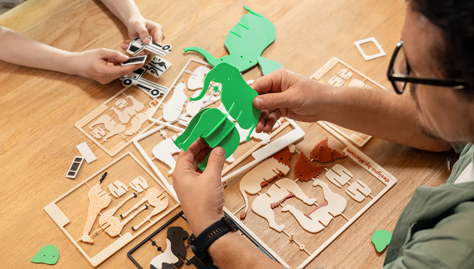 Hands assembling colourful flat printed animals on a wooden worktable.