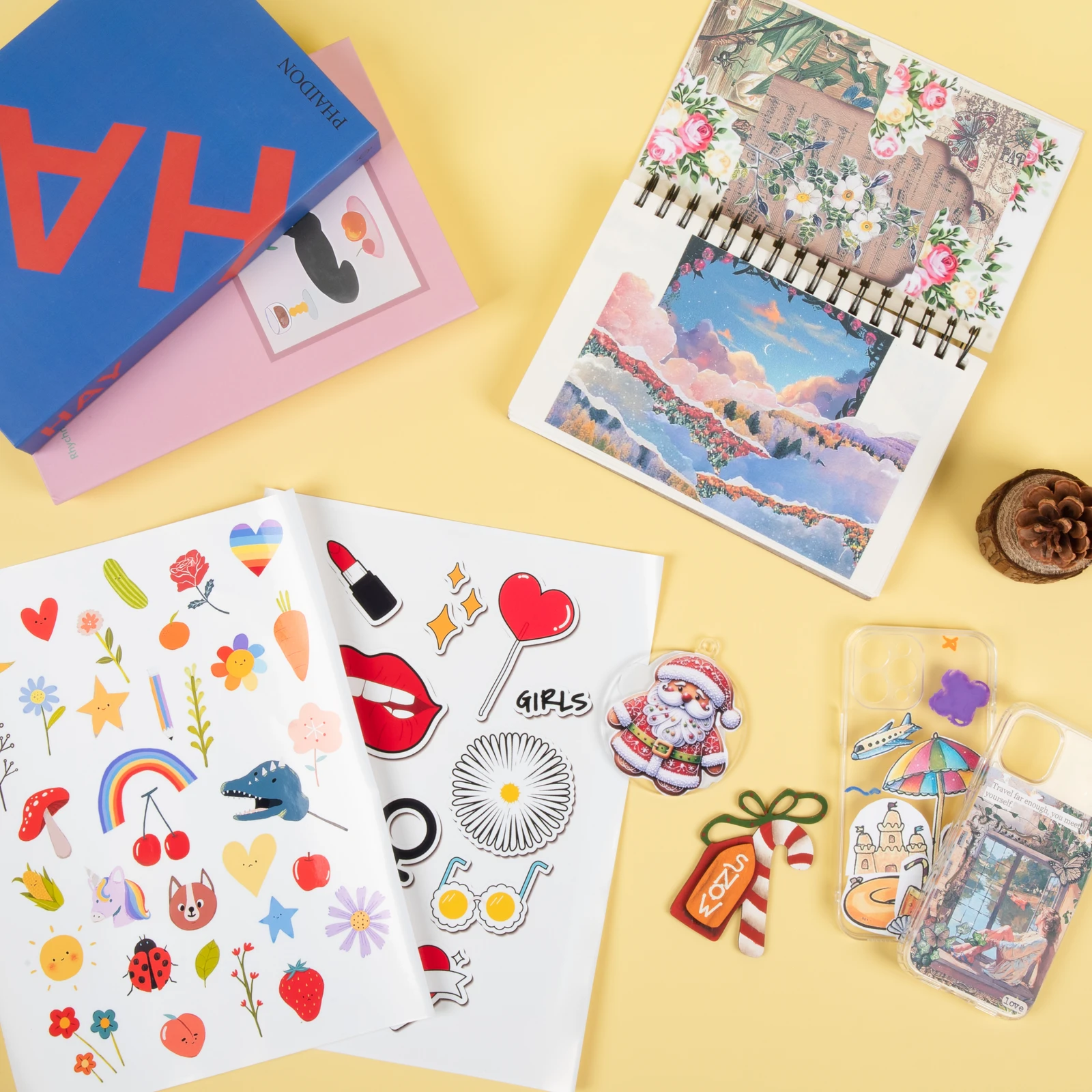 Colourful printed stickers, a decorated notebook and phone cases arranged on a yellow background.
