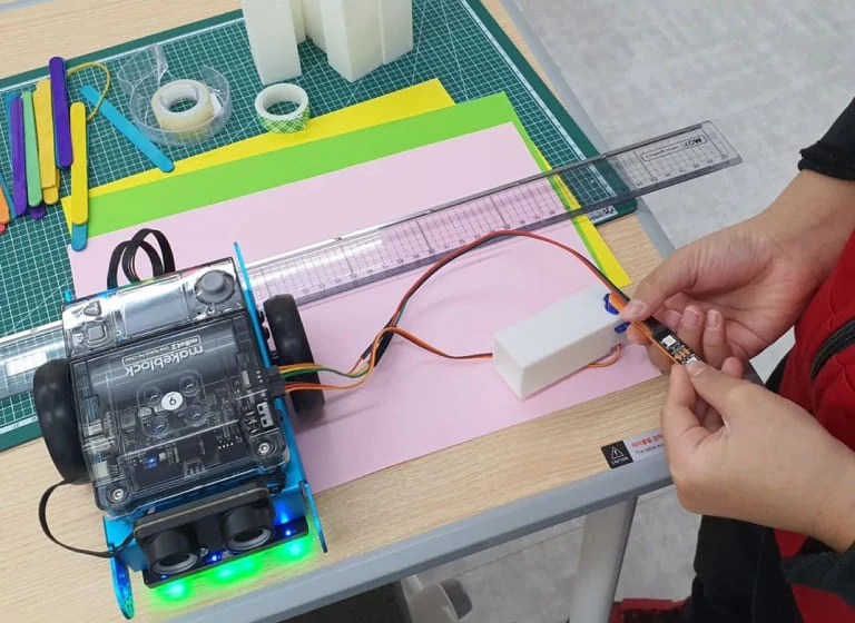 mBot2 on a classroom work surface beside rulers, card and a hands-on project.