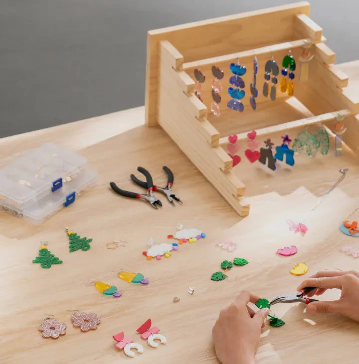Hands assembling small jewellery and accessory pieces at a bright workbench.