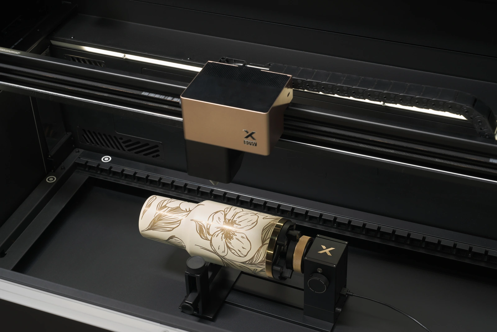 An xTool rotary holding a decorated tumbler inside a laser machine.